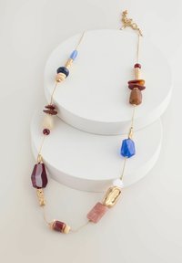 Collier en perles présentant des formes diverses dans des tons rouges, bleus et dorés, avec une chaîne dorée et des accents métalliques texturés.
