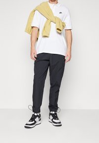 Valkoinen polo-paita mustalla logolla, yhdistettynä tummiin cargo-housuihin. Keltainen villapaita solmittuna hartioiden ympäri ja mustavalkoiset tennarit.