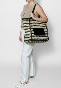 Borsa a tote intrecciata a righe nere e crema con un pannello nero solido, dotata di manici neri robusti e un ampio interno per una grande capacità di stoccaggio.