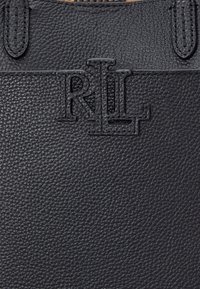 Melnas teksturētas ādas rokassoma ar izspiestu RL logotipu. Virsma ir akmens faktūras ar gludām, pastiprinātām rokturām.