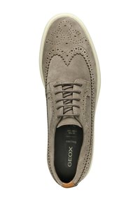 Chaussure en daim gris avec des détails de brogue, bout rond, fermeture à lacets et semelle en caoutchouc blanche. Présente un accent tan au niveau du talon.