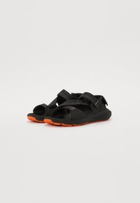 Schwarze Sandalen mit verstellbaren Riemen, ausgestattet mit einer orangefarbenen Gummisohle. Das Design verfügt über ein strukturiertes Riemenmuster und ein robustes Fußbett.