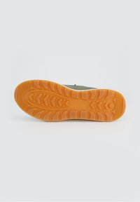 Schuhsohle mit einem strukturierten Design und einem Zickzackmuster aus orangenem Gummi. Der glatte obere Teil aus grünem Synthetik ist oberhalb der Sohle sichtbar.