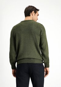 Suéter verde de punto con textura acanalada en los hombros y los puños. Cuenta con un escote redondo y se combina con pantalones oscuros.
