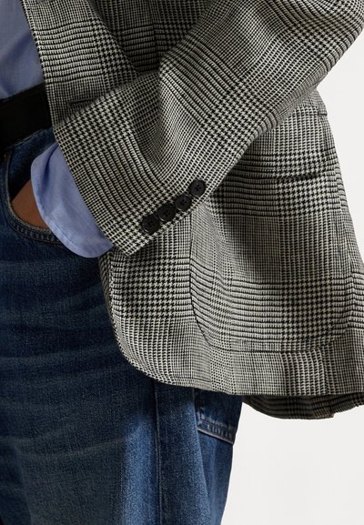 Mustat ja valkoiset houndstooth-kuviolliset bleiserit, joissa on teksturoitu kangas, notched-lapel ja neljä mustaa nappia hihassa.