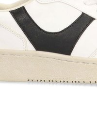 Zapatilla blanca con detalles en cuero negro y suela de goma texturizada en crema. Presenta un diseño contrastante y un acabado suave.