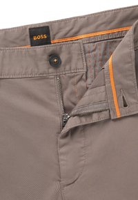 Pantalons gris avec une finition lisse, dotés d'une fermeture éclair devant, d'une fermeture à bouton et d'accents orange. La doublure intérieure présente un motif de logo subtil.
