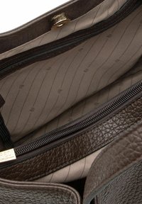 Interno di una borsa in pelle marrone testurizzata con una fodera beige liscia, caratterizzata da un compartimento con cerniera e dettagli in metallo dorato.