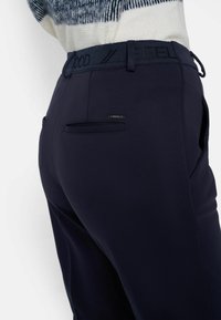 Marinblå byxor med en slät textur, med en midjeband där "FEEL GOOD" är präglat, samt två bakfickor med minimala metalldetaljer.