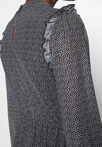 Czarna sukienka w białe kropki, przezroczysty materiał, akcenty z falbanami na rękawach, detal w kształcie klucza na plecach oraz marszczona tekstura w talii.