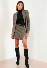 Brun houndstooth blazer med skræddersyet pasform, sort ribbet polotrøje, matchende nederdel med side split og knæhøje sorte ruskinds støvler.