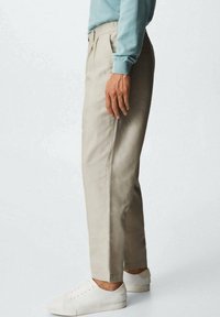 Beige katoenen broek met een rechte snit, voorzien van zijzakken en lichte plooien, gecombineerd met witte sneakers en een lichtblauwe trui.