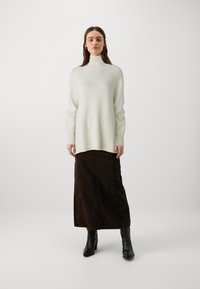 Pull en col roulé couleur crème avec des manches longues, assorti à une jupe en denim ajustée marron foncé et des bottes à talons hauts noires.