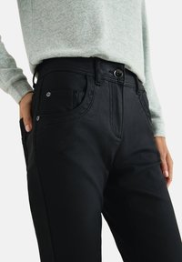 Sorte denimbukser med en tætsiddende pasform, featuring knaplukning, forlommer og diskrete syninger. Sammen med en let sweater.