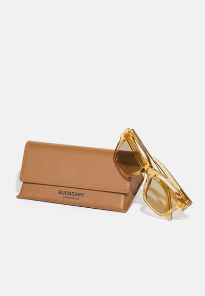 Burberry-Sonnenbrille mit einem gelben transparenten Rahmen, begleitet von einem braunen Ledergehäuse mit geprägter Markenbeschriftung.