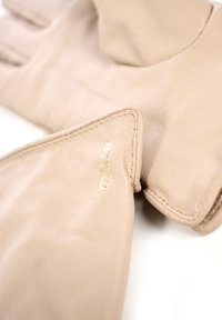 Beige læderhandsker med syede kanter, der har en tekstureret overflade og et diskret gyldent logo på manchetten.