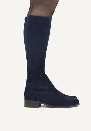 Legs wearing dark blue suede knee-high boots with low block heels against a plain light background.