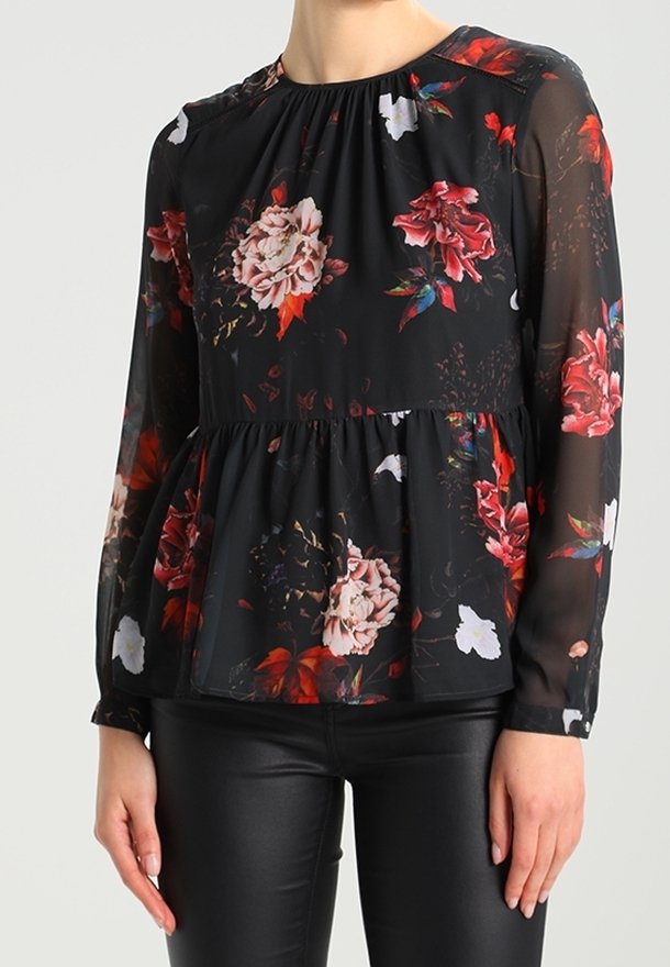Blouse noire transparente à manches longues avec imprimé floral rouge, rose et blanc, taille peplum, portée avec un pantalon en cuir noir.