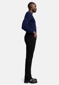 Navy gebreide trui, zwarte spijkerbroek en zwarte veterschoenen. De spijkerbroek zit strak om het lichaam, heeft een gladde textuur en minimale details.