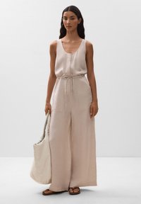 Helles beiges Jumpsuit mit weiten Beinen, lockerer Passform und verstellbarem Bindegürtel. Dazu eine gesteppten, creamfarbenen Schultertasche.