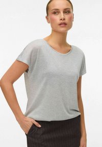 T-shirt gris clair à manches courtes, col rond, tissu doux, coupe décontractée, associé à une jupe noire à rayures, main dans la poche.