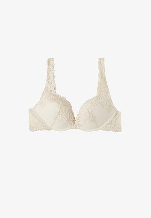 Beige lace bra with padded cups, textured fabric, wide lace-trimmed straps, and scalloped edges. Features smooth band and floral accents.