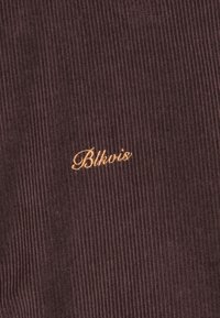 Brown corduroy fabric with vertical ribs; features "Blkvis" embroidered in gold. Fuzzy texture with a rich, deep color.