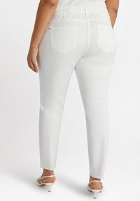 Białe dopasowane spodnie z elastycznym paskiem, dwoma tylnymi kieszeniami i gładką teksturą. W połączeniu z sandałami na obcasie z odkrytymi palcami.