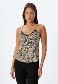 Top de tirantes con estampado de leopardo y borde de encaje negro, tirantes ajustables, tejido suave y corte relajado. Leggings negros completan el conjunto.