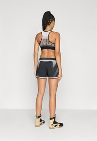 Calções atléticos pretos com painéis laterais em rede, combinados com um top de desporto preto e branco com costas em tule. Usados com sapatilhas altas bege e pretas.