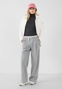 Giacca imbottita bianca, dolcevita grigia, pantaloni ampi grigio chiaro con coulisse e cappellino rosa con logo. Sneaker casual completano il look.