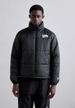 Schwarze Pufferjacke mit hohem Kragen, Reißverschluss und sichtbaren Nähten. Sie verfügt über ein Logo auf der Brust und den Bündchen mit elastischen Anpassungen.