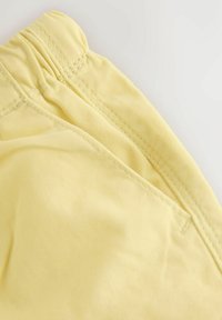 Yellow fabric shorts with an elastic waistband, featuring a smooth texture and neat stitching details.