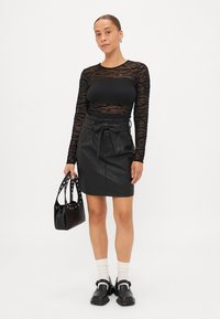 Μαύρη μπλούζα με μακριά μανίκια και διαφανείς υφασμάτινες λεπτομέρειες, συνδυασμένη με μαύρη δερμάτινη φούστα ψηλόμεση με ζώνη που δένεται. Μαύρη τσάντα και παπούτσια.