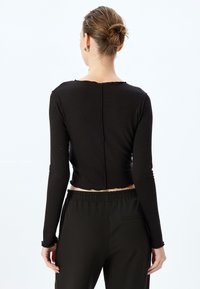 Zwarte cropped top met lange mouwen, voorzien van een onafgewerkte zoom en een lichte structuur. Gecombineerd met zwarte broek met elastische taille en een zijzak.