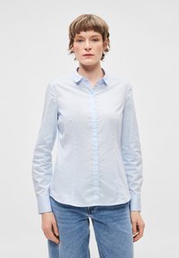 Svetlomodrá košeľa s golierom, dlhými rukávmi, zapínaním na gombíky vpredu a jemne prispôsobeným strihom. Vyrobená z hladkej látky s minimálnymi detailmi.