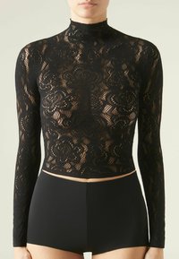 Top in pizzo nero a maniche lunghe con colletto alto, caratterizzato da intricati motivi floreali e un design cropped, abbinato a pantaloni shorts neri a vita alta.