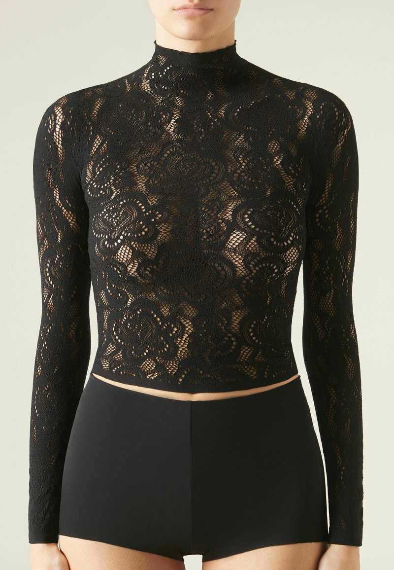 Top in pizzo nero a maniche lunghe con colletto alto, caratterizzato da intricati motivi floreali e un design cropped, abbinato a pantaloni shorts neri a vita alta.