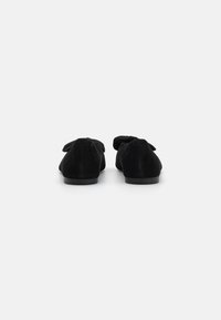 Pantofi negri din suede cu vârf rotunjit, având un detaliu cu fundă pe spate și o talpă plată. Textură simplă și netedă.