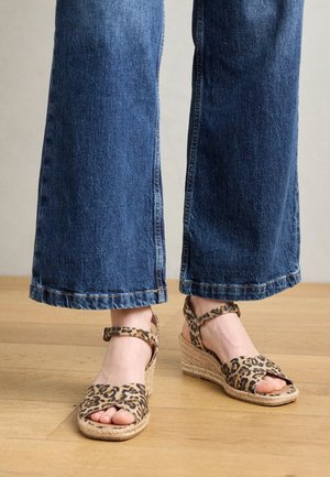 Sandały na koturnie w panterkę z espadrylową podeszwą i paskiem na kostce, zestawione z dżinsami w szerokich nogawkach w kolorze niebieskim.