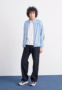 Light blue jacket, black accents, paired with a white shirt, black pants featuring subtle patterns, and white/black sneakers.