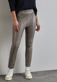 Harmaat tekonahkahousut, joissa on slim fit -leikkaus, paneelityöstö ja korkea vyötärö, yhdistettynä valkoisiin lenkkikengiin.