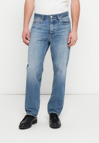 Ανοιχτό μπλε τζιν παντελόνι με άνετη γραμμή, φθαρμένες λεπτομέρειες, σχεδιασμό με πέντε τσέπες και κλείσιμο με κουμπιά. Συνδυάζεται με μαύρα παπούτσια.