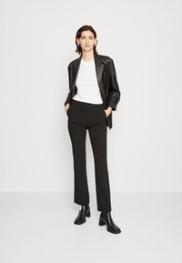 Jachetă de piele neagră peste o cămașă albă, asociată cu pantaloni negri adaptați și cizme cu toc negre, la gleznă. Design minimal și siluetă modernă.