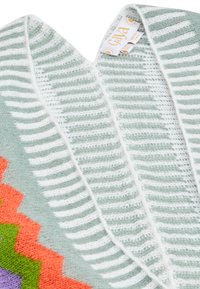 Puloverul tricotat are un design cu decolteu în V de culoare verde deschis, cu dungi albe și modele zigzag multicolore în nuanțe de portocaliu, violet și verde.