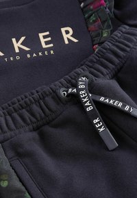 Granatowy sweter z logo w kolorze złotym, kwiatowymi akcentami i sznurkiem z nadrukowanym tekstem. Miękka tkanina i elastyczny detal w pasie.