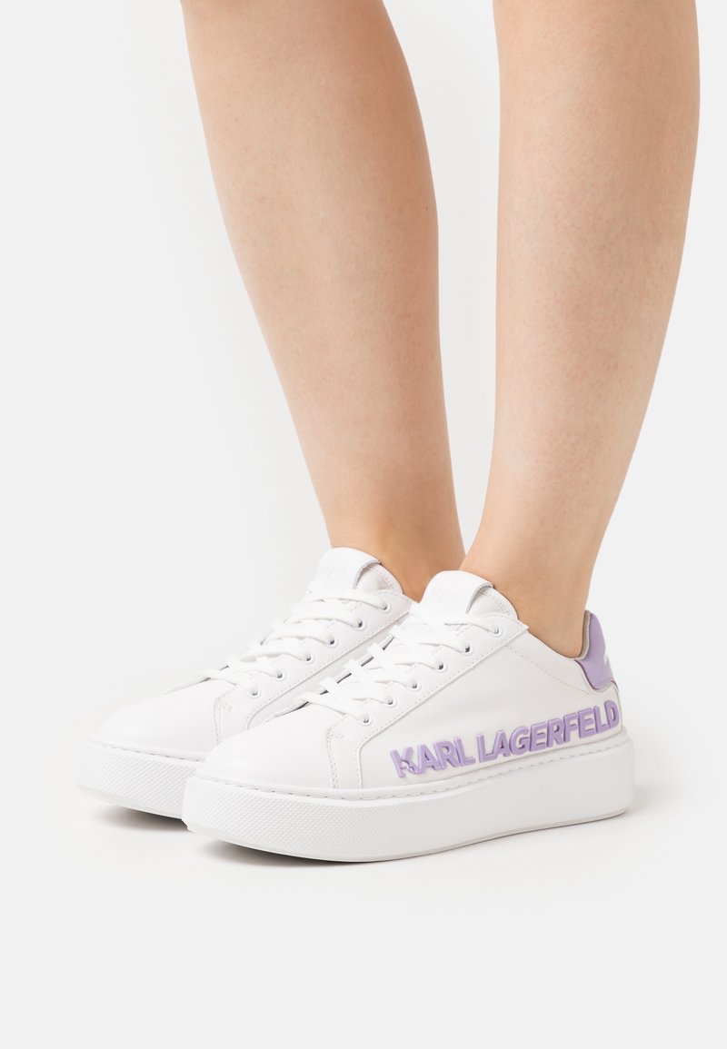 Baskets compensées blanches avec des touches de lavande et le logo "KARL LAGERFELD", portées pieds nus sur un fond uni.