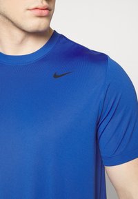Královsky modré sportovní tričko vyrobené z syntetického materiálu, s černým logem Nike na hrudi, kulatým výstřihem a krátkými rukávy.