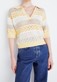 Žlutý a bílý pruhovaný krátký rukáv pletený svetr s výstřihem do V a límečkem, který má otevřenou texturu v diamantovém vzoru.