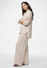 Completo beige a due pezzi con texture, composto da una camicia a maniche lunghe e pulsanti morbida e pantaloni a gamba larga, abbinato a sandali neri con tacco.